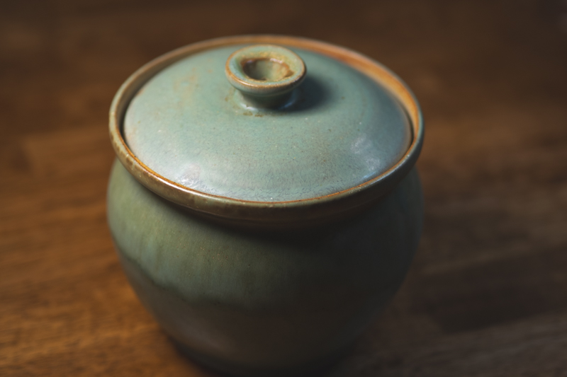 A round lidded jar in pale celadon green with a small knob and amber rim.