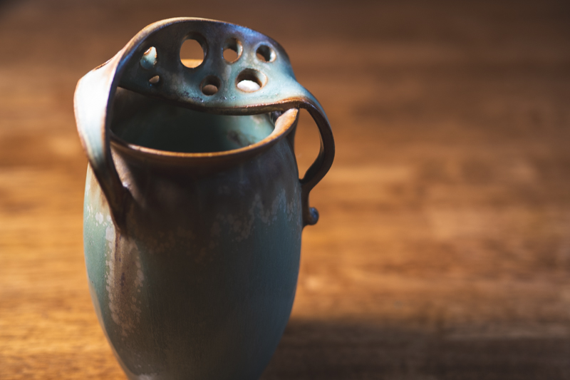 A celadon vessel seen head-on, its pierced lid folded and resting inside the rim.