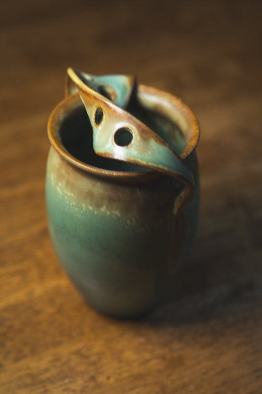 A tall celadon-glazed vessel with a pierced, folded lid that rests inside the rim.