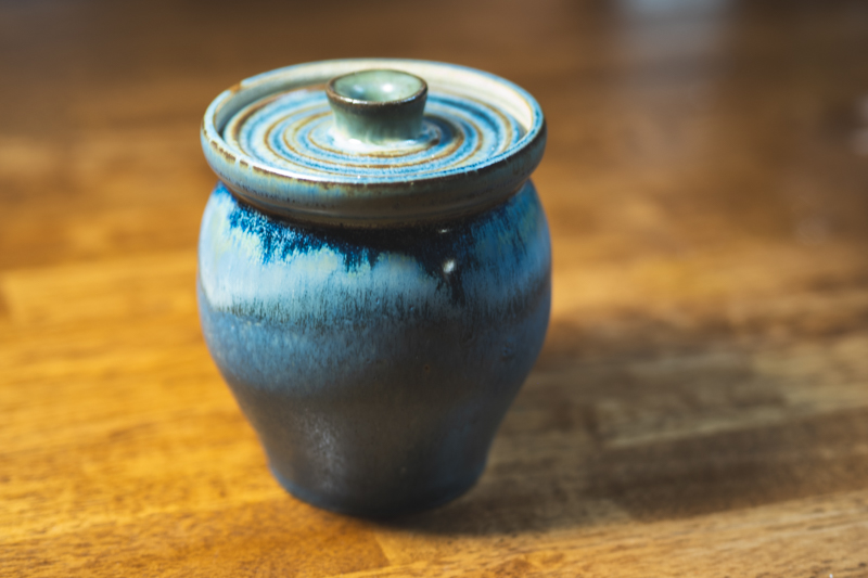 A rounded lidded jar with a ridged lid, glazed in layered slate blue and cream.