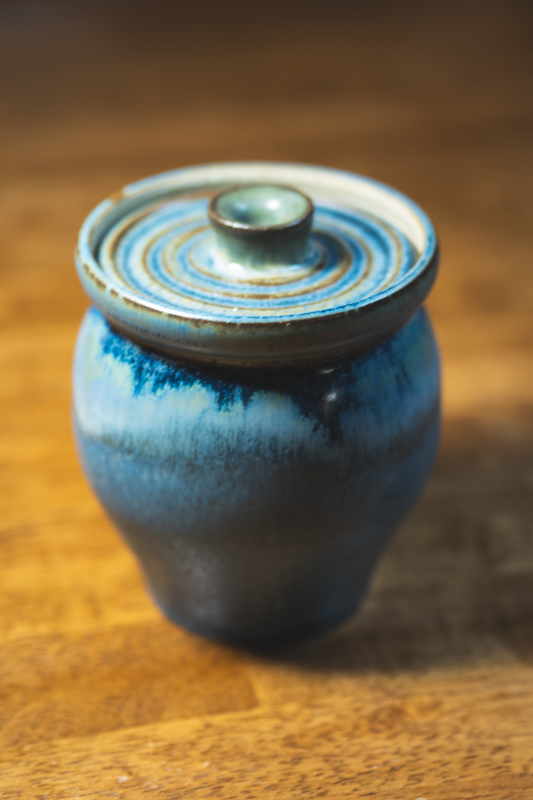 A ridged-lid jar glazed in slate blue and cream, standing in warm light.