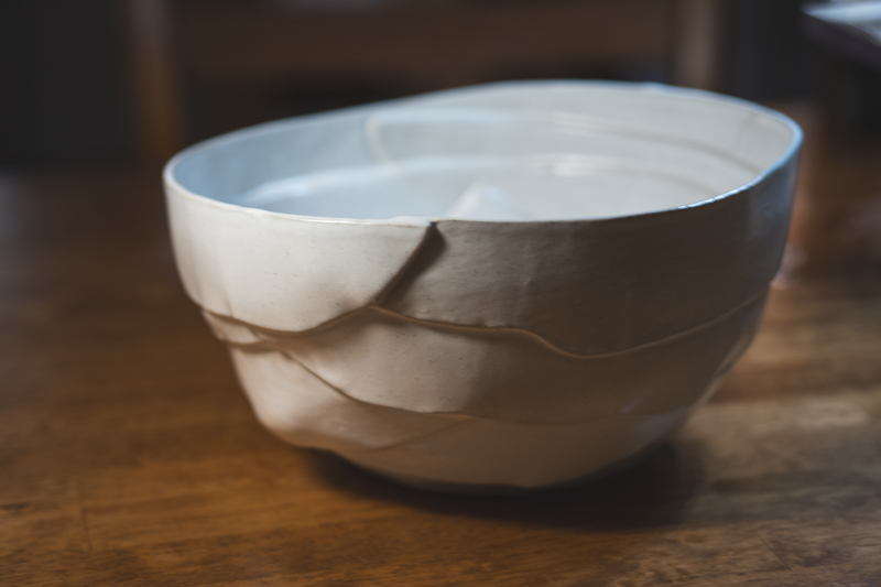 A white faceted bowl seen from the side, with slab seams visible on its surface.