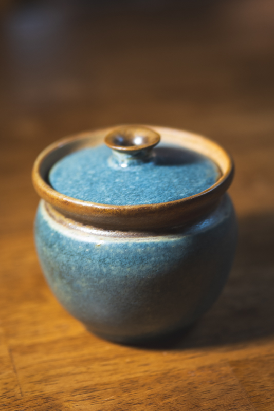 A small round lidded jar in indigo with an amber rim, seen from slightly above.