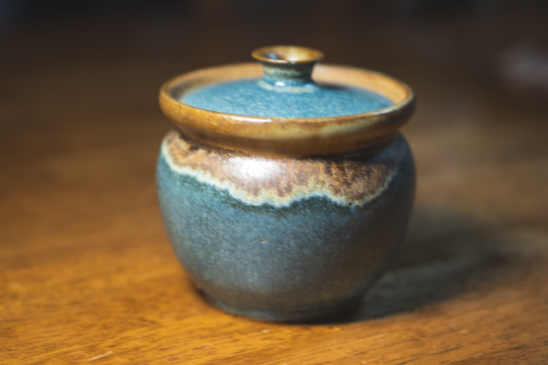 A squat lidded jar glazed in deep indigo with an amber-brown rim and lid edge.