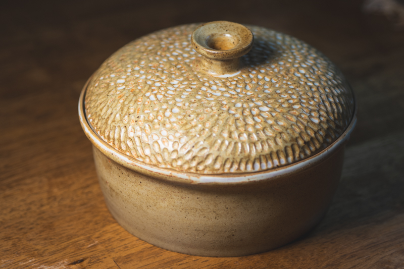 A lidded casserole with a domed lid carved in a dense, radiating texture, glazed in honey ochre.