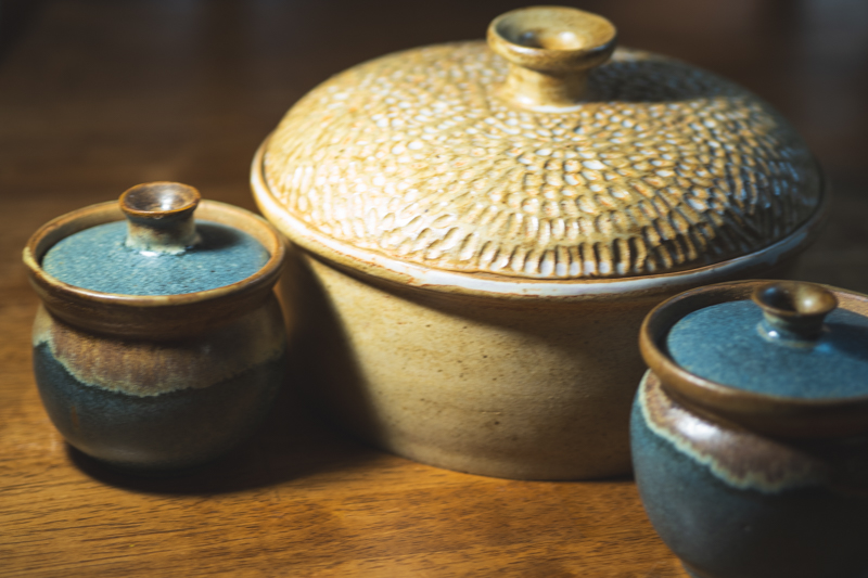 A carved casserole flanked by two small indigo jars on a walnut table.
