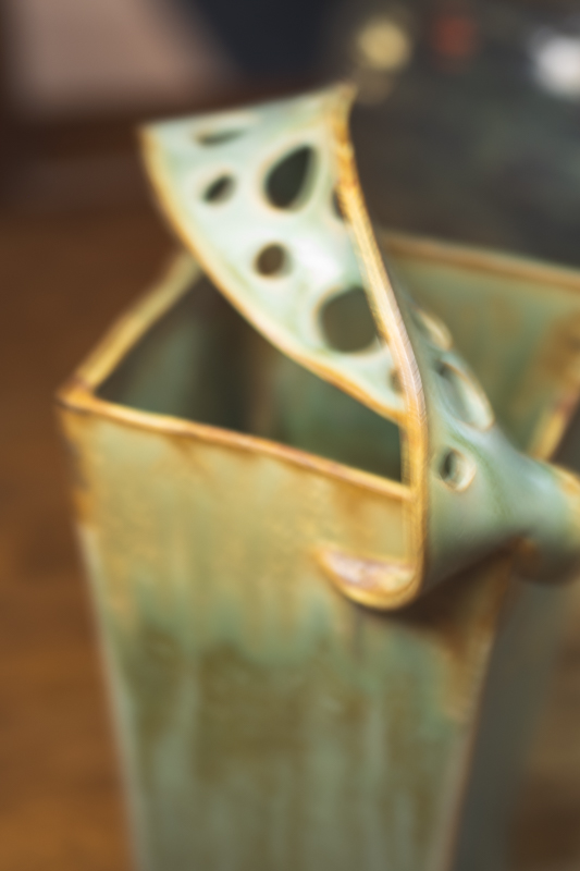 Close detail of a square vase's pierced lid, glazed in sage with an amber edge.