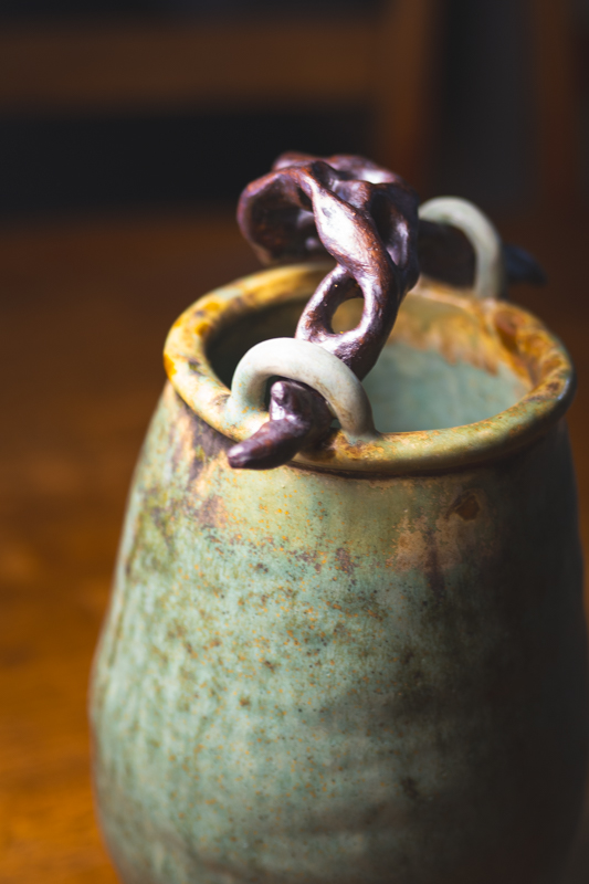 A tall mottled green vessel with a twisted, root-like sculpted form rising from the rim.