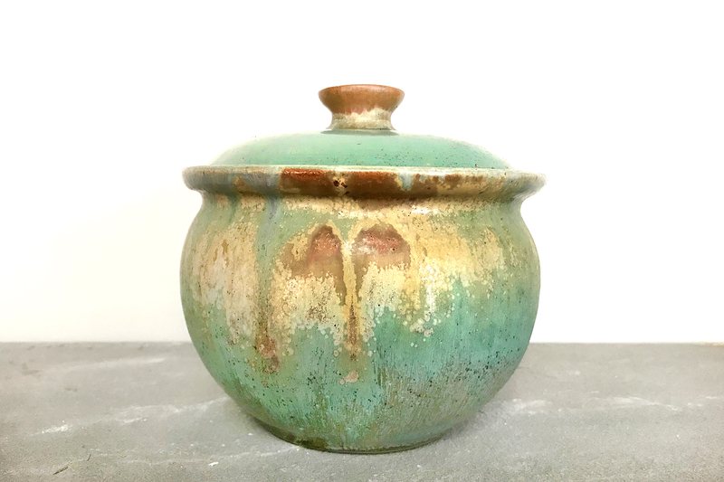A round lidded canister glazed in mottled verdigris green with amber at the rim and knob.