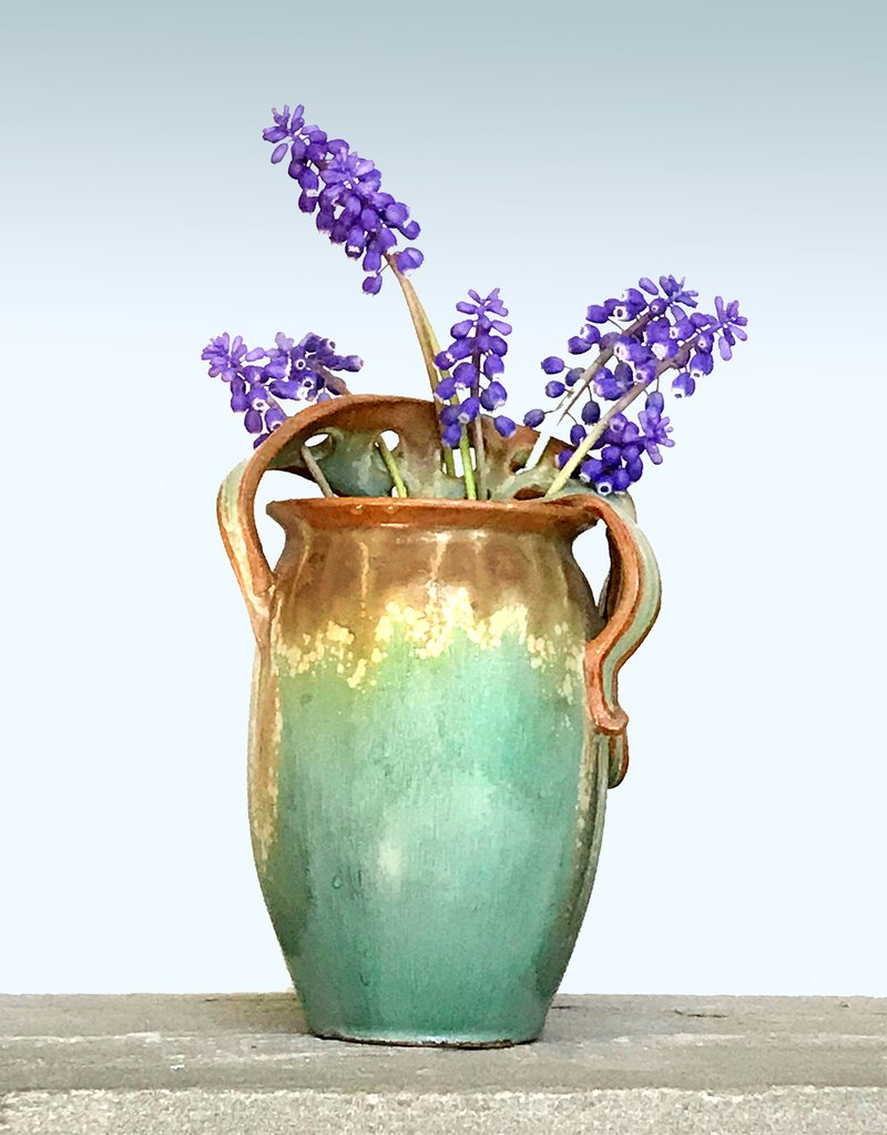 A tall two-handled vase glazed in verdigris green with amber at the rim, holding grape hyacinth.