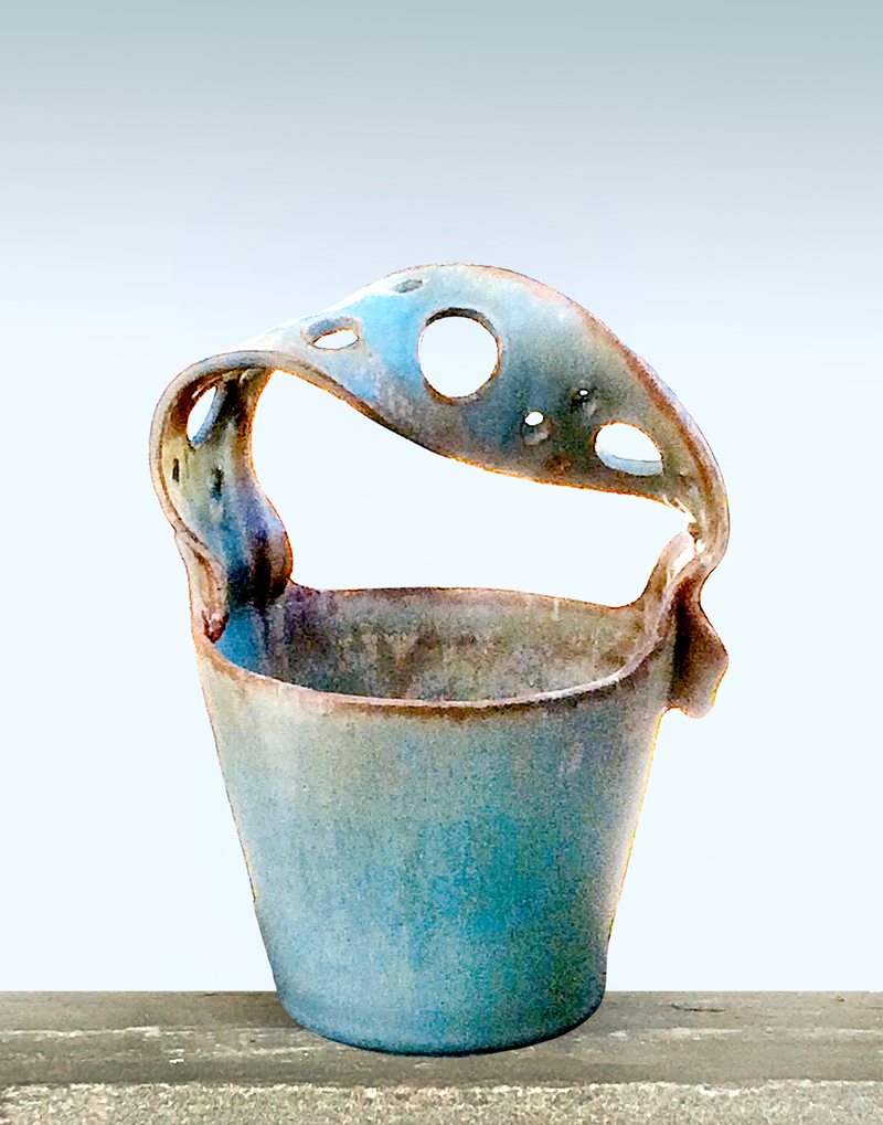 A basket-shaped vase with a wide pierced strap handle arching over the top, glazed in verdigris green.