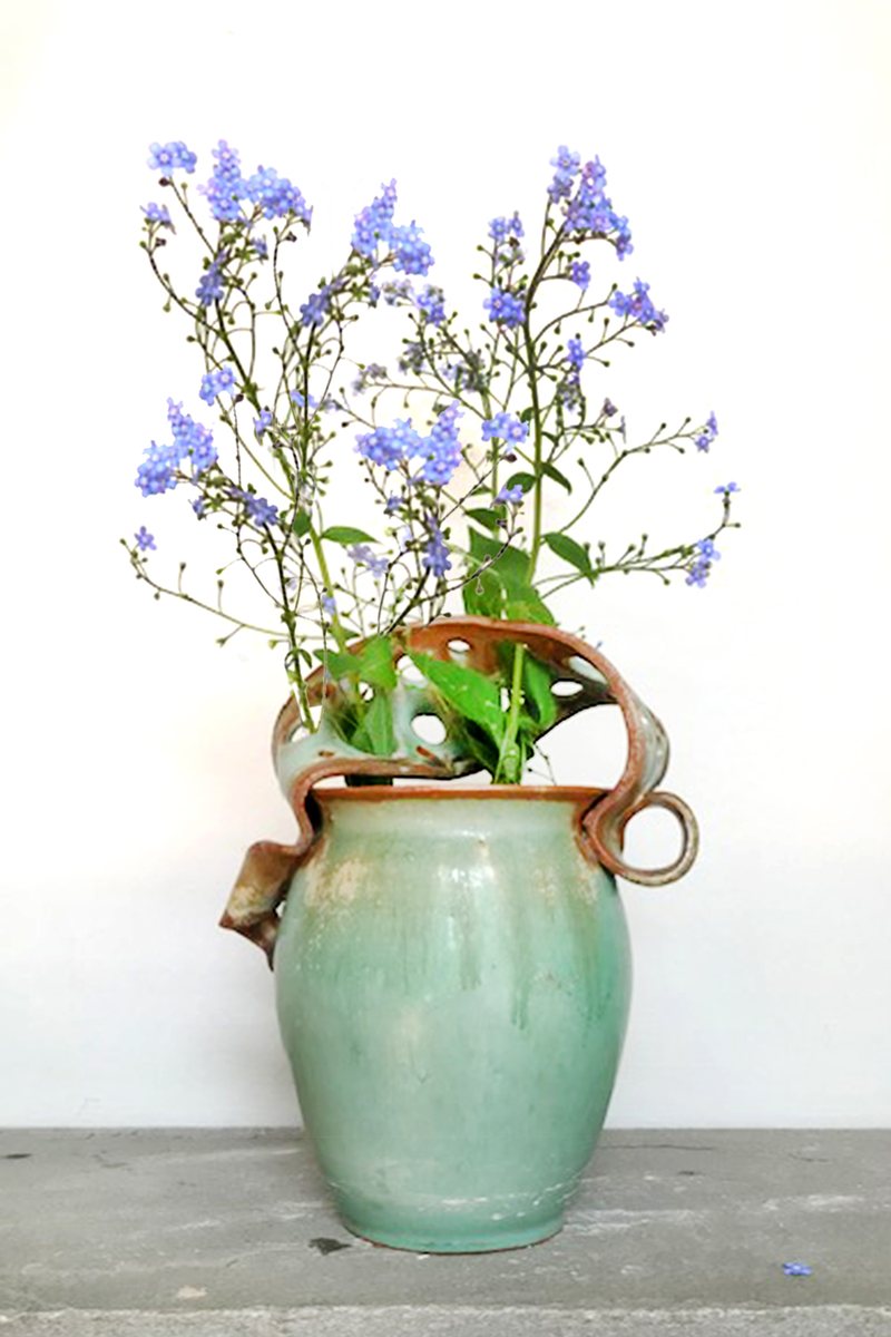 A verdigris vase whose rim folds and curls outward, holding a spray of forget-me-nots.